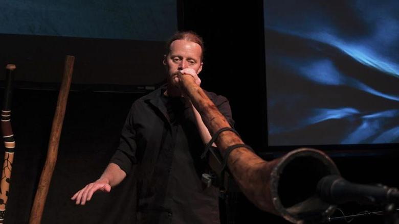 A person playing a didgeridoo into a microphone